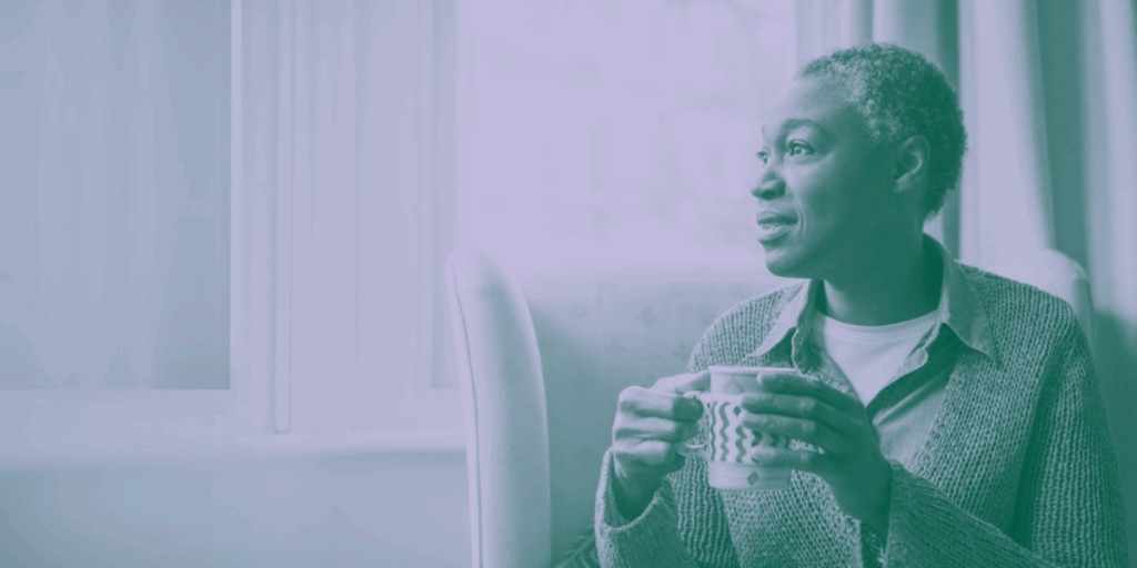 Woman sitting and drinking a cup of coffee while looking happily out of the window.