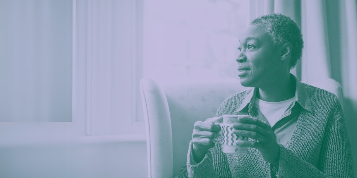 Woman sitting and drinking a cup of coffee while looking happily out of the window.