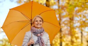 a portrait of happy senior woman with umbrella at autumn park