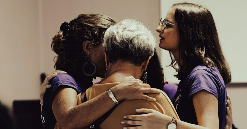 4 women standing in a circle with their arms around each other in support