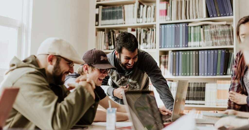 3 men sitting at a desk looking at their laptop screens and laughing