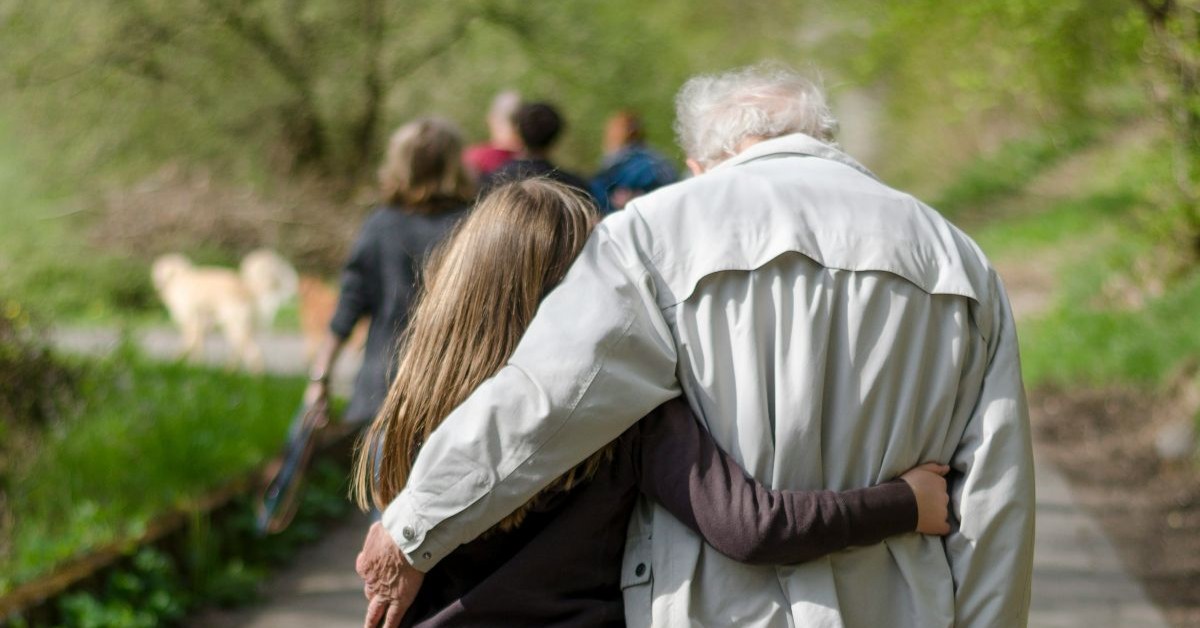 Intergenerational support. An older man and high granddaughter walking through the park together, supporting eachother.