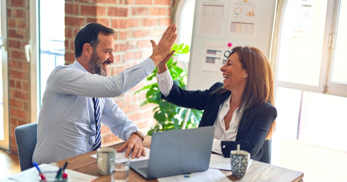 A man and a woman working at a desk high fiving each other and smiling