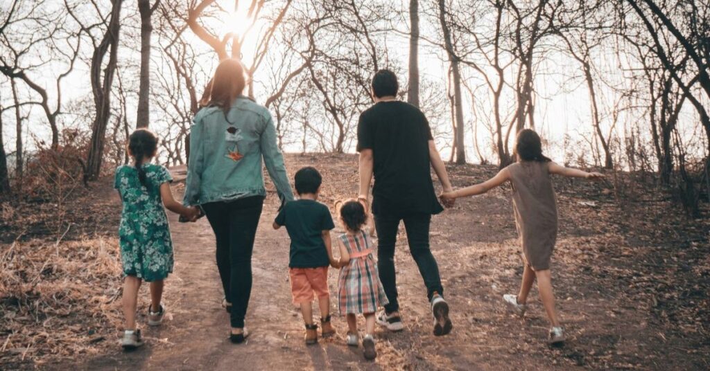 A family of 6 - Mum, Dad and 4 children, holding hands facing the sun.