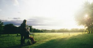 Woman walking, pushing an elderly woman in a wheelchair through the fields with the sun shining.