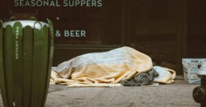 A person sleeping on the street under blankets as they are homeless.