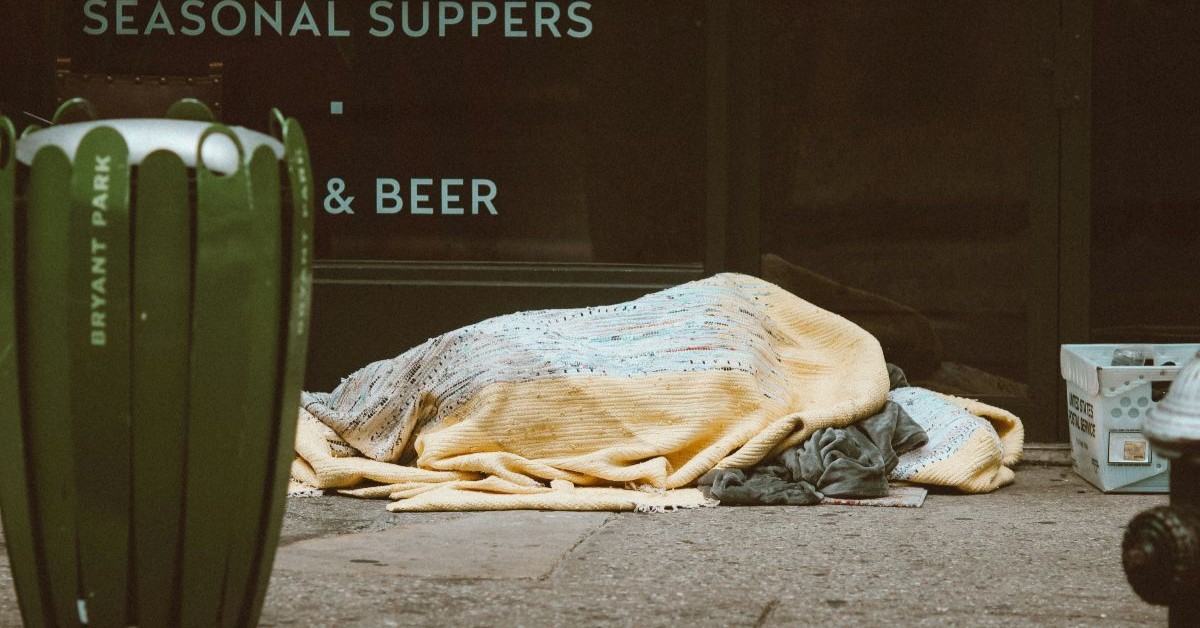 A person sleeping on the street under blankets as they are homeless.