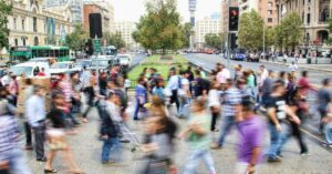 A crowd of people, that look blurry as they all walk past each other quickly in the street.